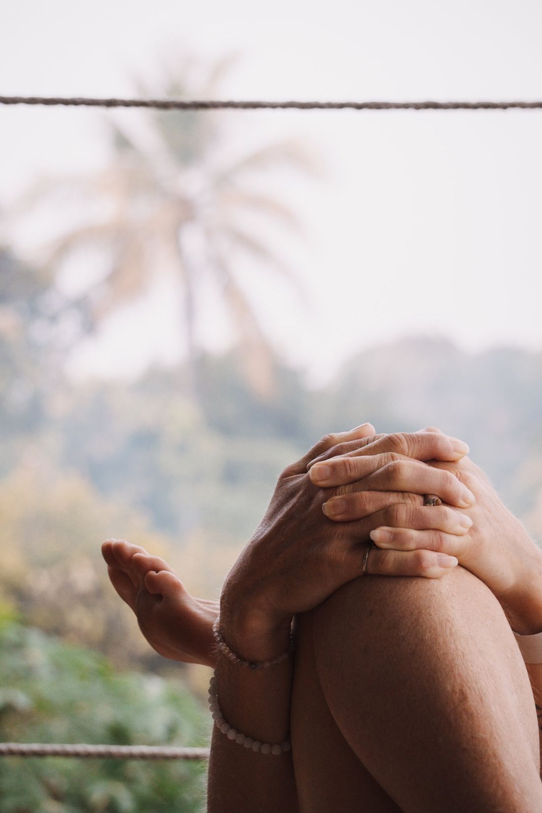 Hands clasped around a knee, palm tree softly out of focus