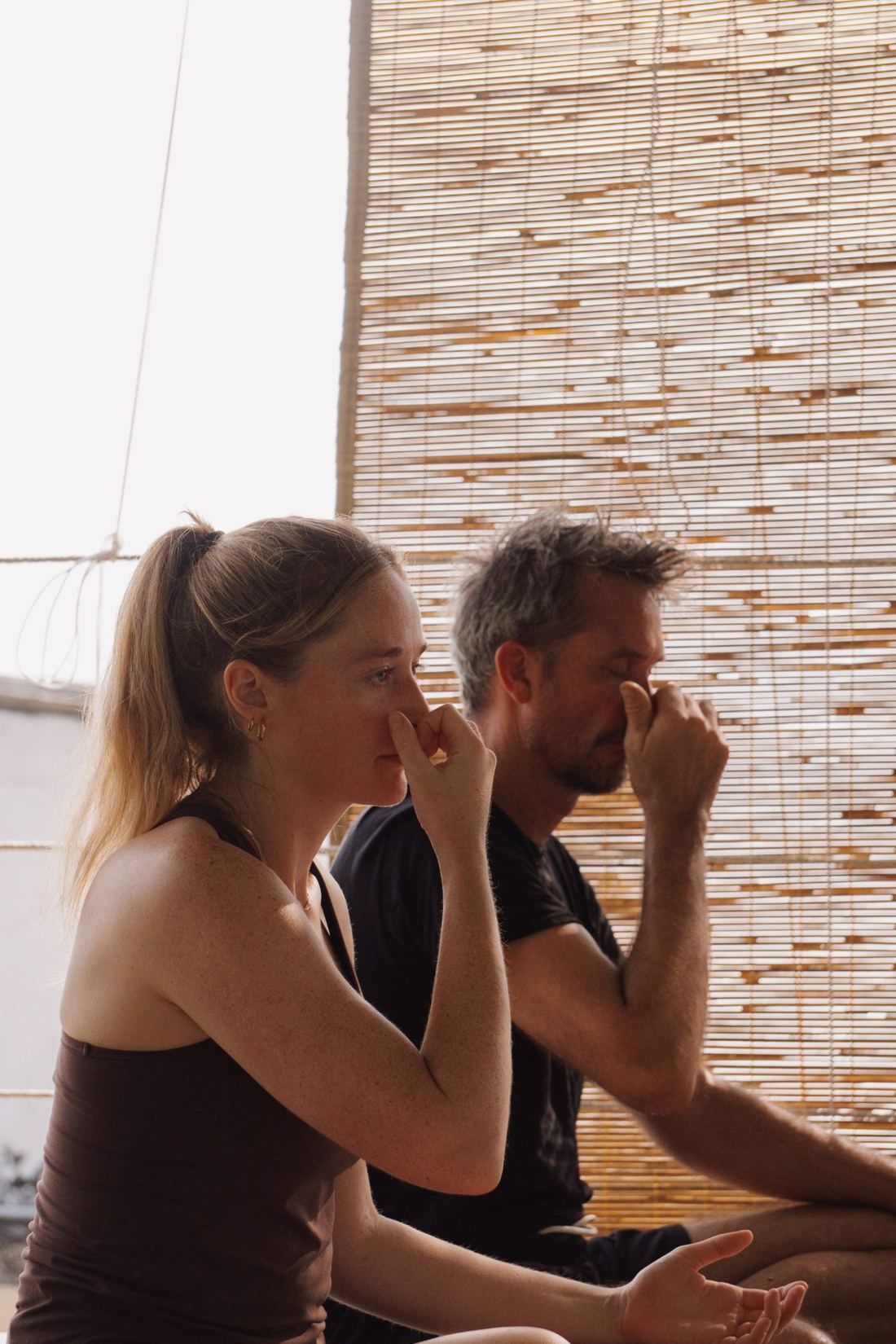 Two students practising alternate-nostril breathing beside a bamboo blind